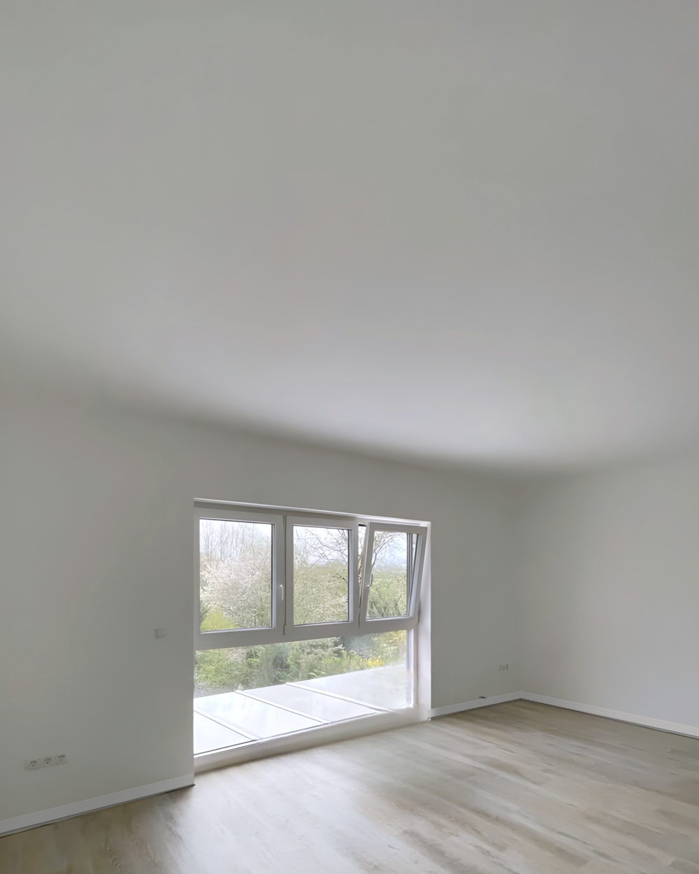 Nachher: heller Wohnraum mit weißen Wänden, Fensterfront und Laminatboden